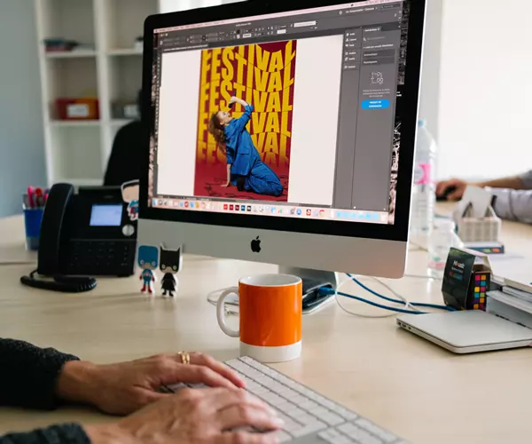 Graphiste retouchant une affiche de festival avec photo de danseuse sur iMac